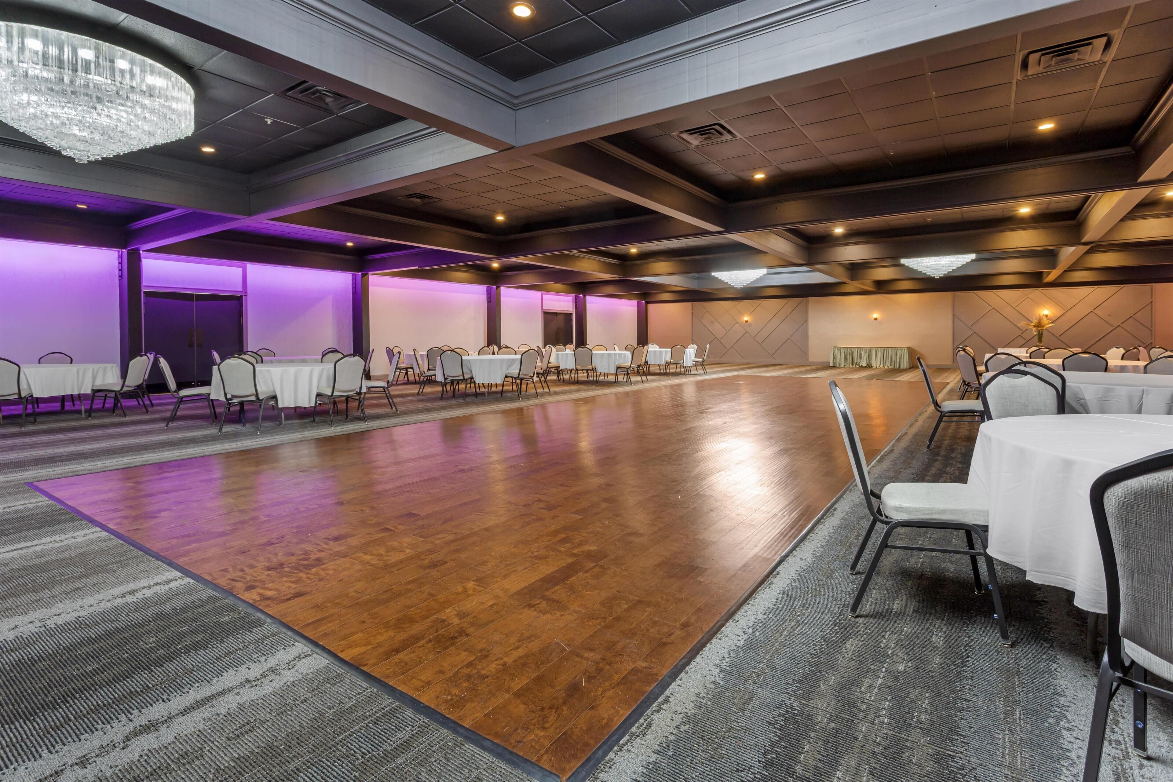 A large conference room with multiple tables and chairs, a wooden floor, and purple ambient lighting.