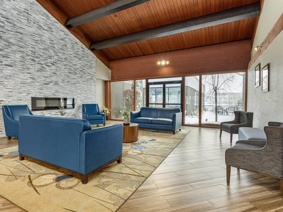 A spacious living area with a stone wall, wooden ceiling beams, and large windows offering a view of the outdoors.