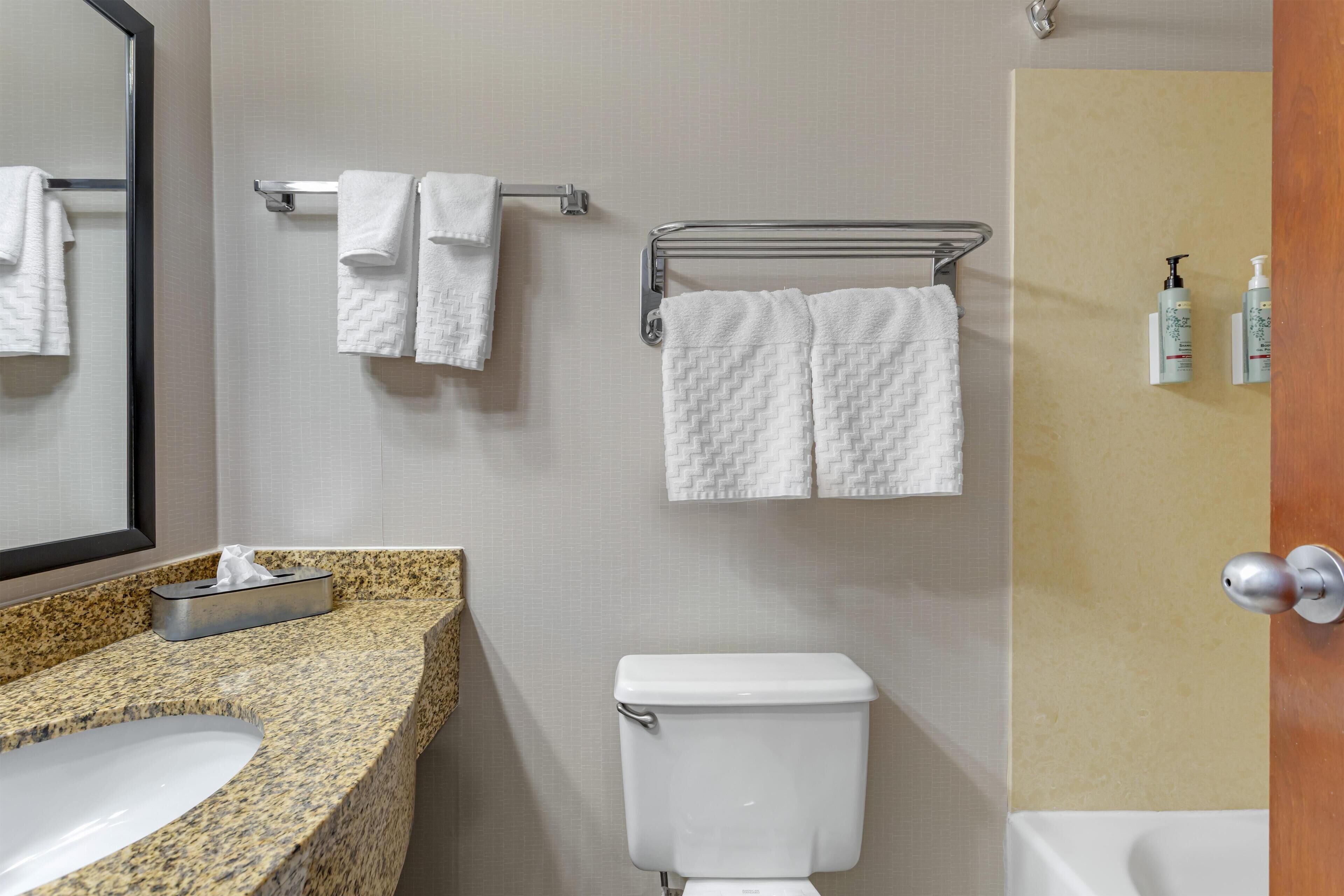 A bathroom with a granite countertop sink, a white toilet, and a towel rack with two towels.