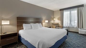 A hotel room with a large bed, two bedside tables with lamps, a chair, and a large window with curtains.
