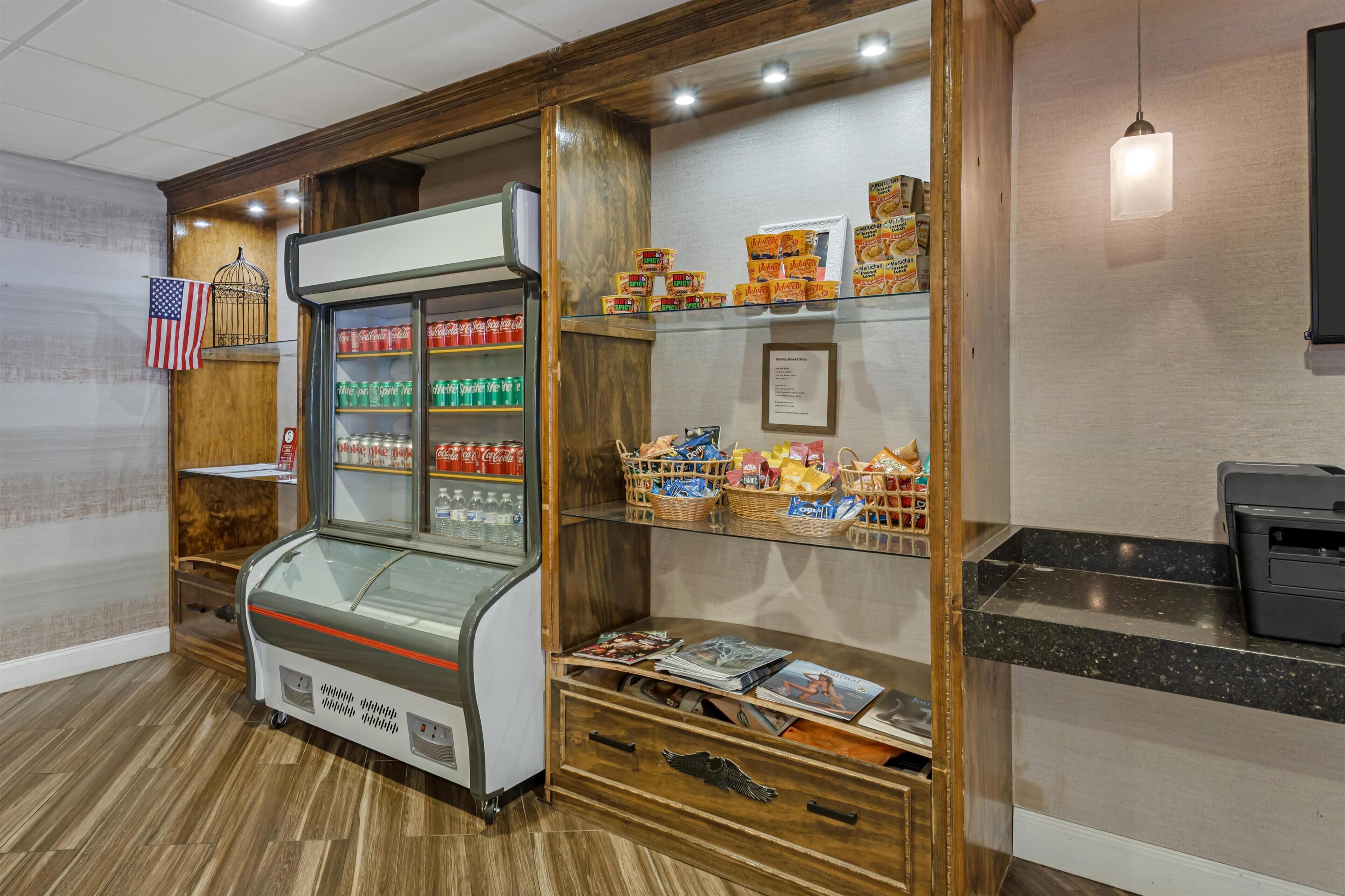 Una estación de autoservicio para bebidas con Coca-Cola y otras opciones, una selección de aperitivos y revistas sobre un mostrador.