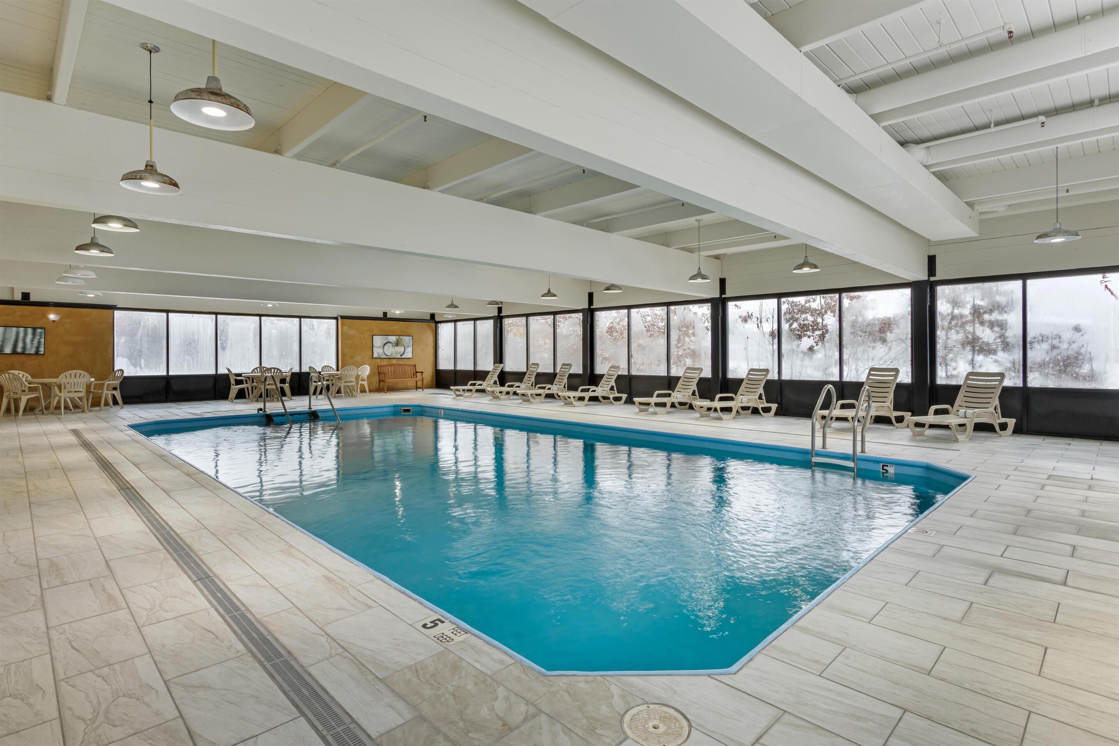 An indoor swimming pool with clear water, surrounded by lounge chairs and a tiled floor.