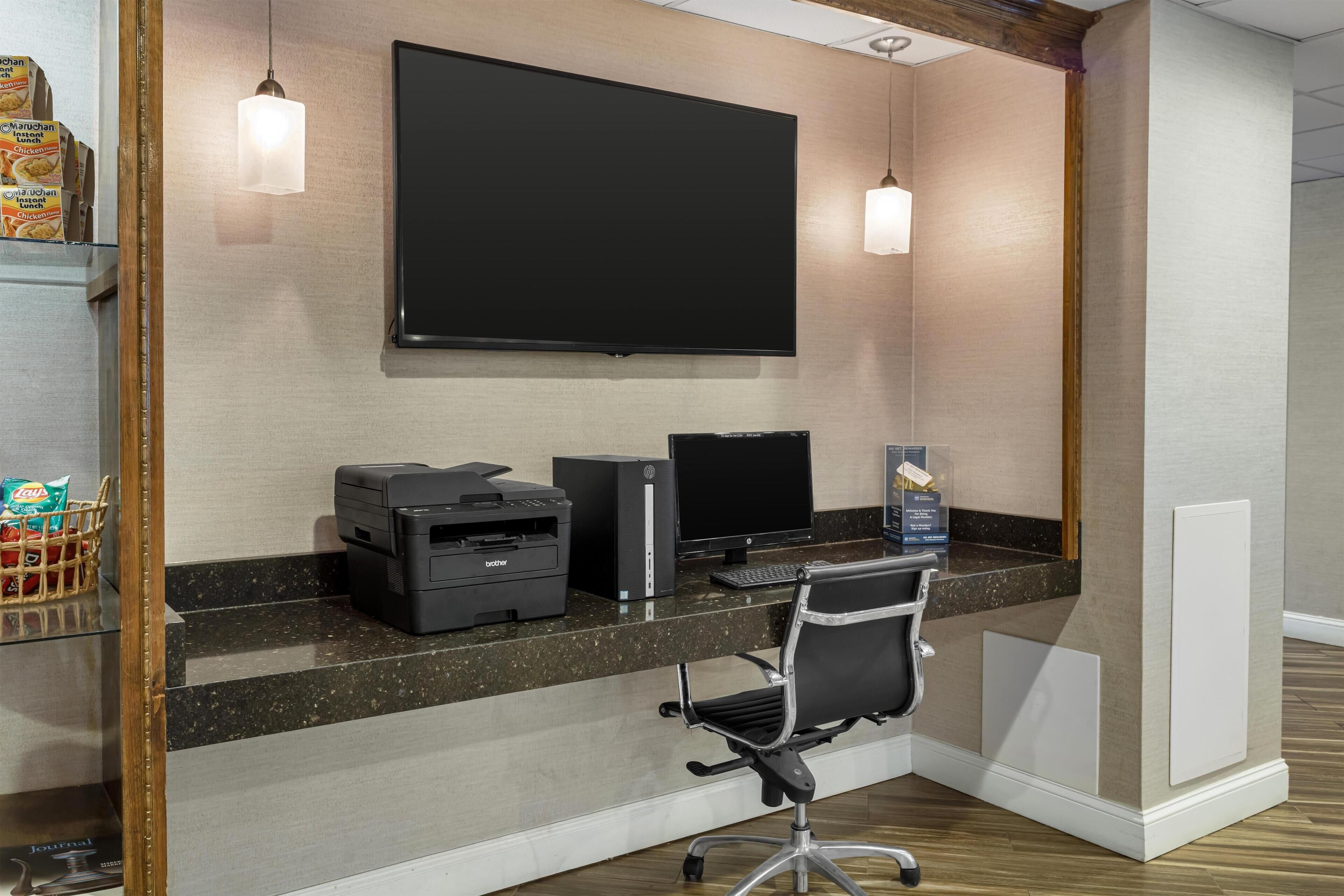 Un espacio de oficina moderno con un monitor de pantalla plana grande, una computadora de escritorio e impresora sobre un escritorio de granito oscuro.