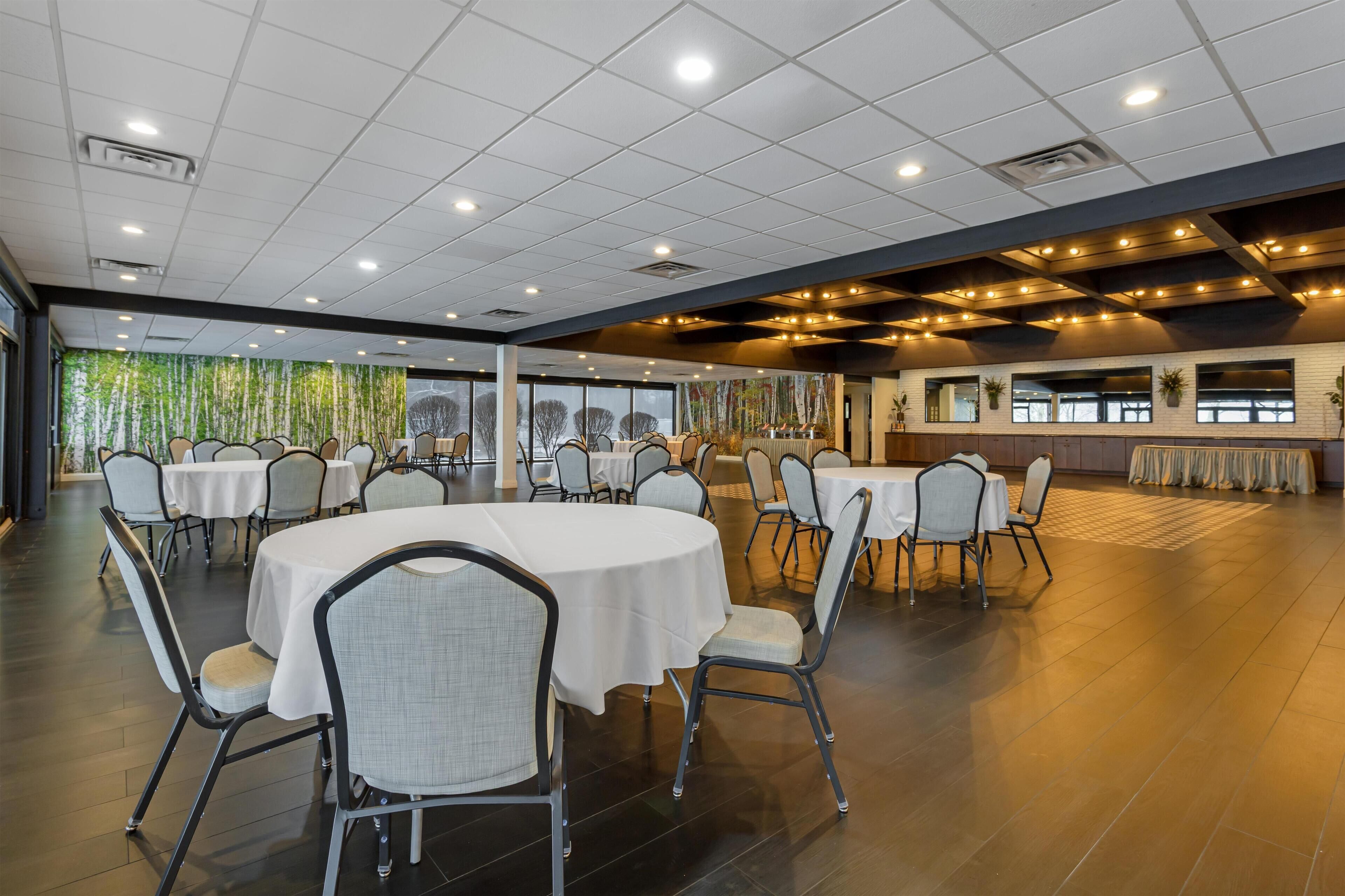 Un amplio comedor interior con mesas y sillas redondas, ventanas grandes y un diseño de techo moderno.