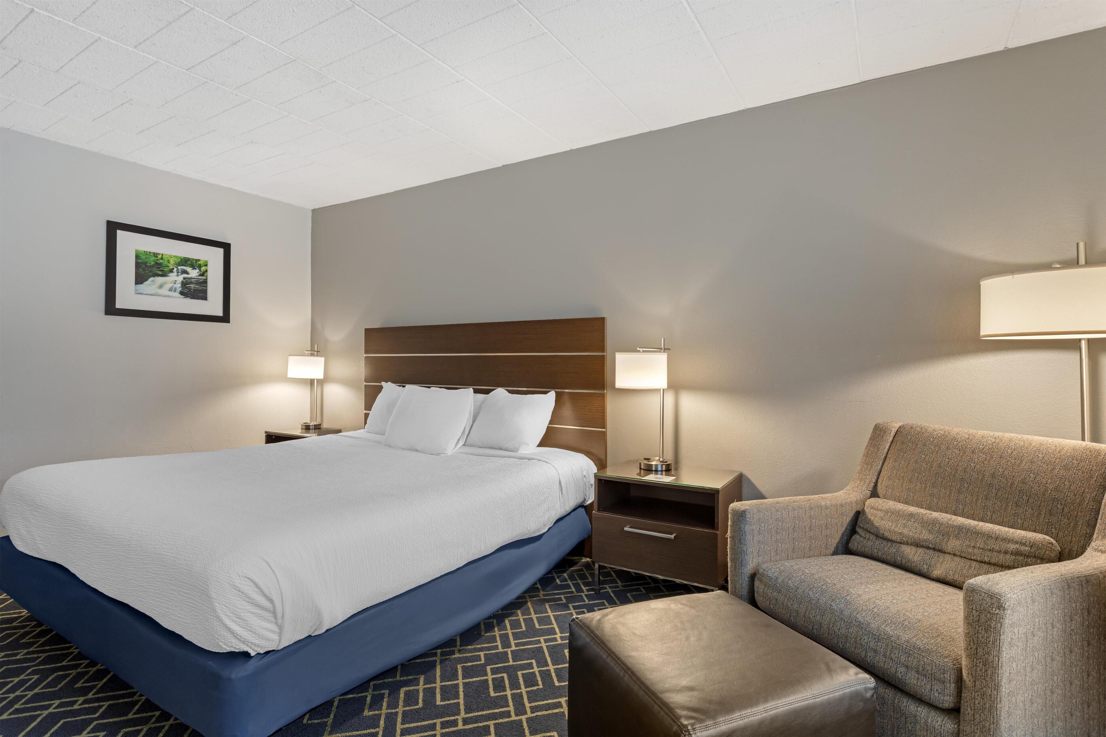 A hotel room with a large bed, two bedside tables with lamps, a chair, and a small ottoman.