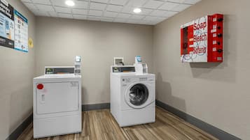 A laundry room with two washing machines, a soap and bleach dispenser, and a wall-mounted control panel.