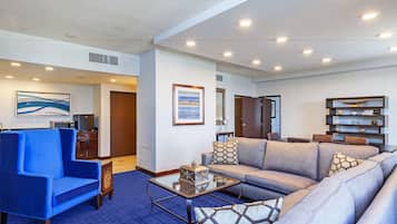 A modern living room with a blue armchair, a grey sofa, and a glass coffee table.