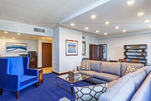 A modern living room with a blue armchair, a grey sofa, and a glass coffee table.