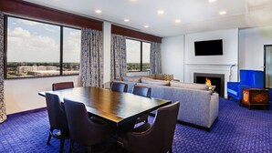 A hotel room with a dining table, chairs, a sofa, a fireplace, and a TV mounted on the wall. - Hilton Waco (Waco)