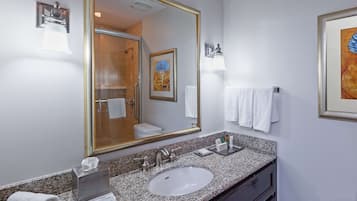 Un baño con un espejo grande, un lavamanos, un perchero para toallas y un cuadro en la pared.