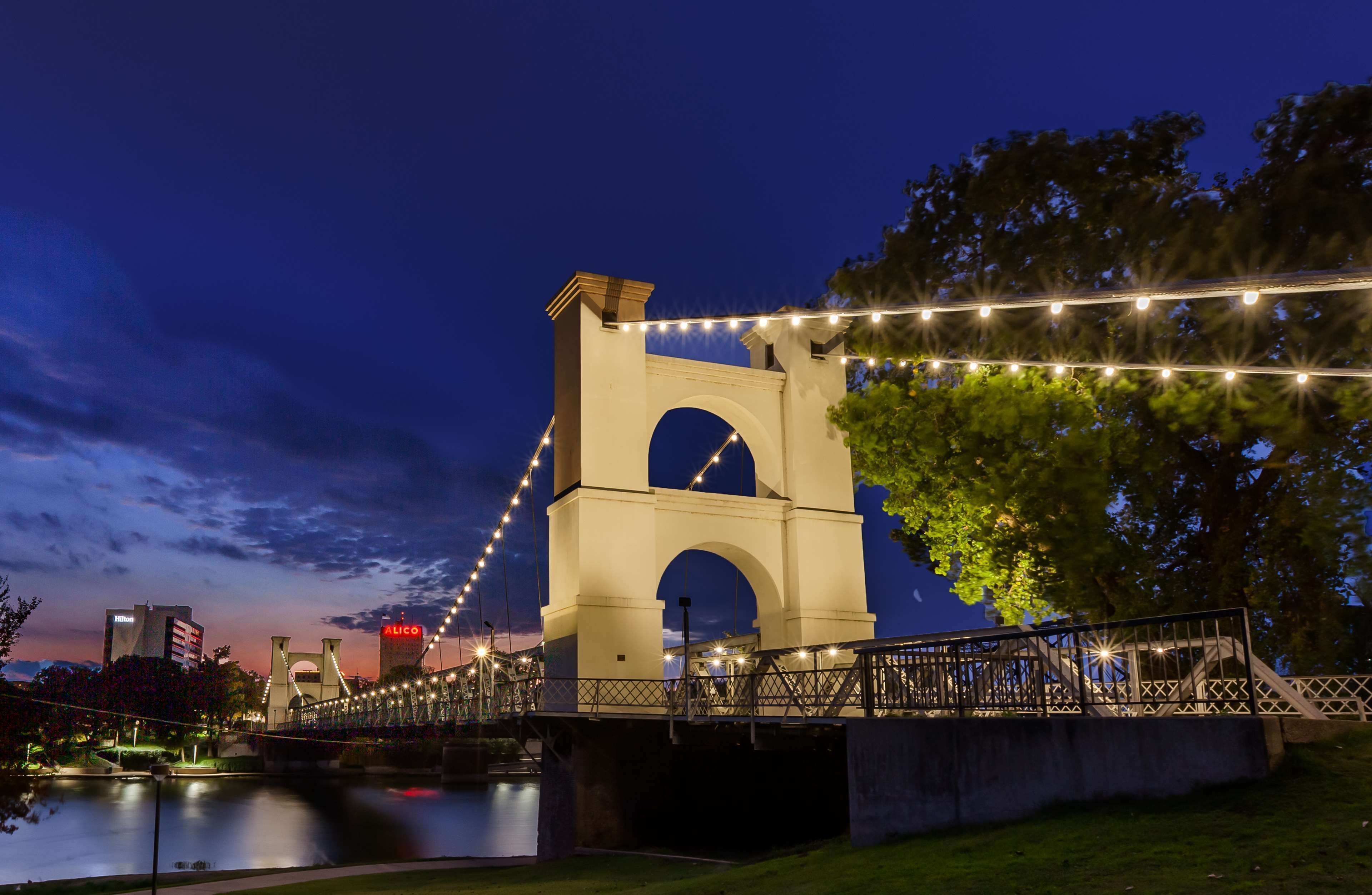 A bridge with a large arch and a railing, surrounded by trees and a body of water.