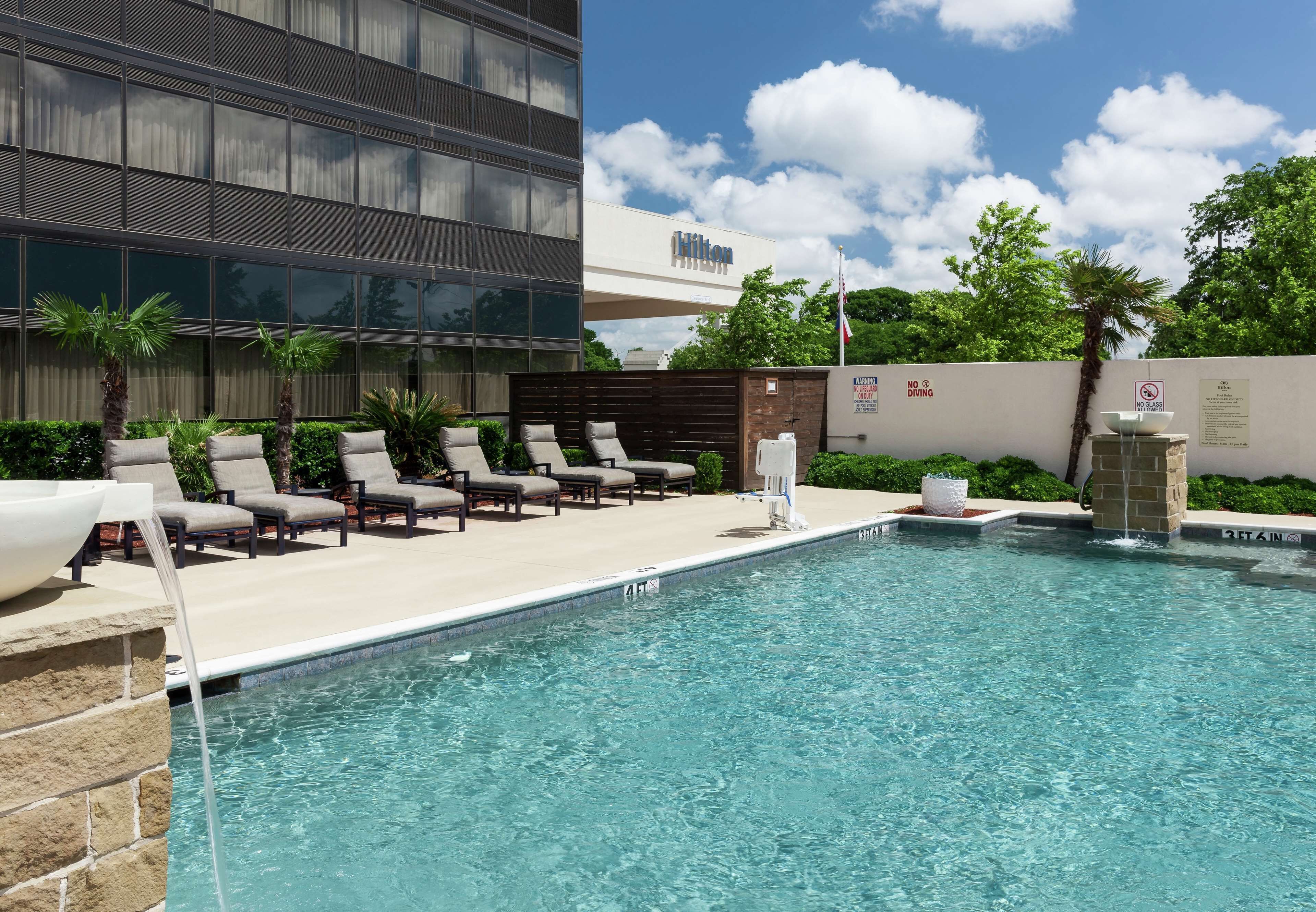 A pool area with lounge chairs, a water feature, and a building with a 'Hilton' sign.