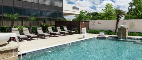 A pool area with lounge chairs, a water feature, and a building with a 'Hilton' sign.