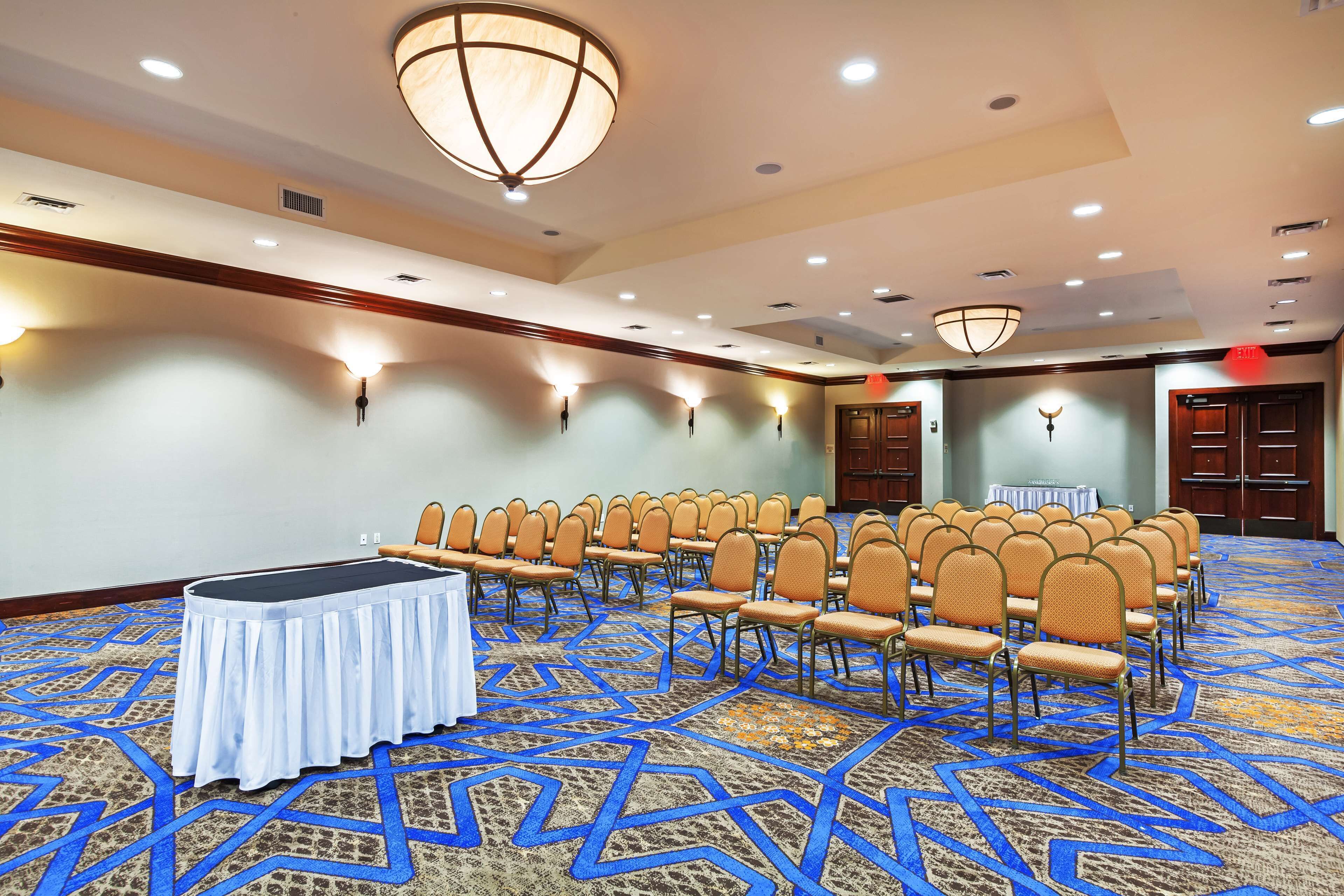 A conference room with rows of chairs, a table, and a patterned carpet.
