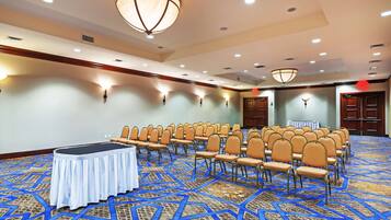 A conference room with rows of chairs, a table, and a patterned carpet.