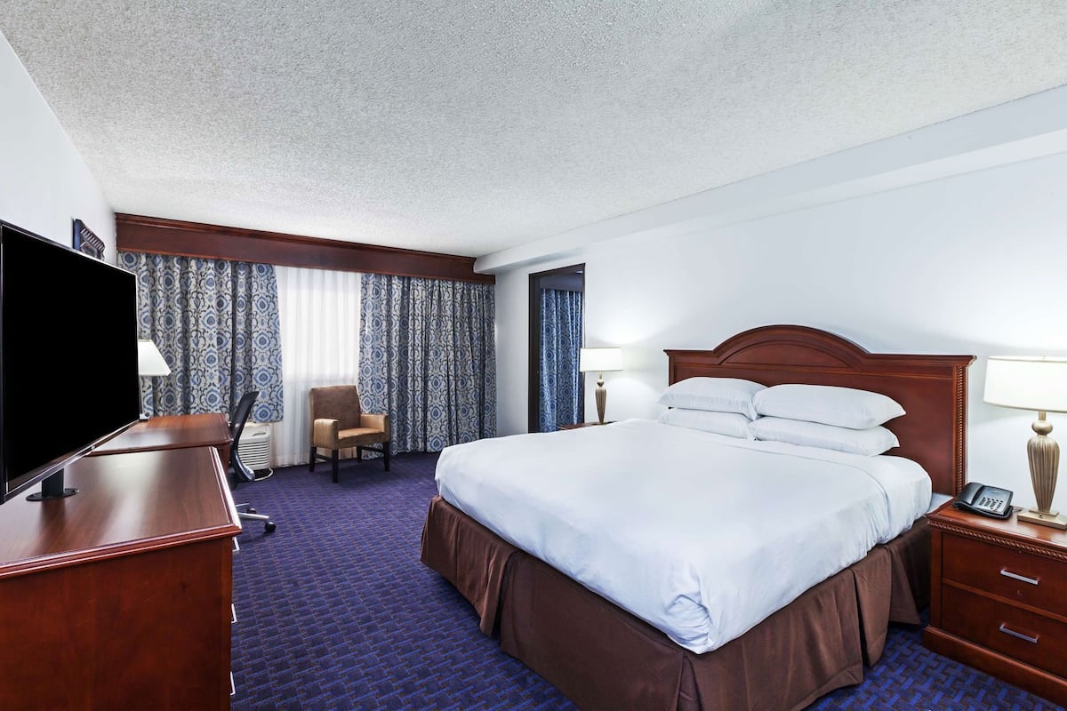 A hotel room with a large bed, a desk with a TV, a chair, and a lamp.