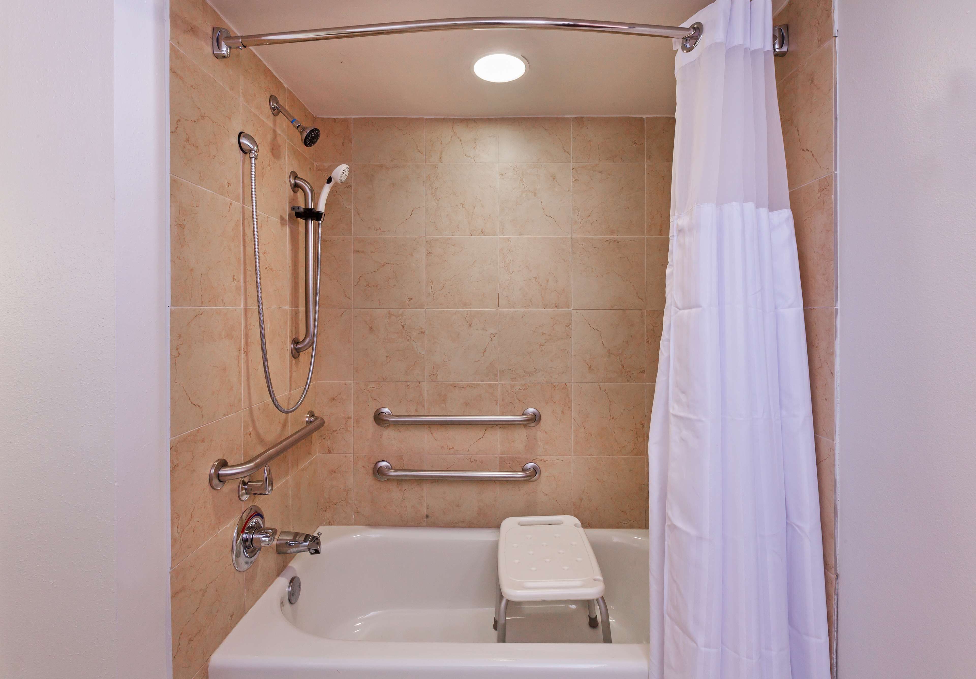 Un baño con bañera, barras de apoyo y cabezal de ducha.