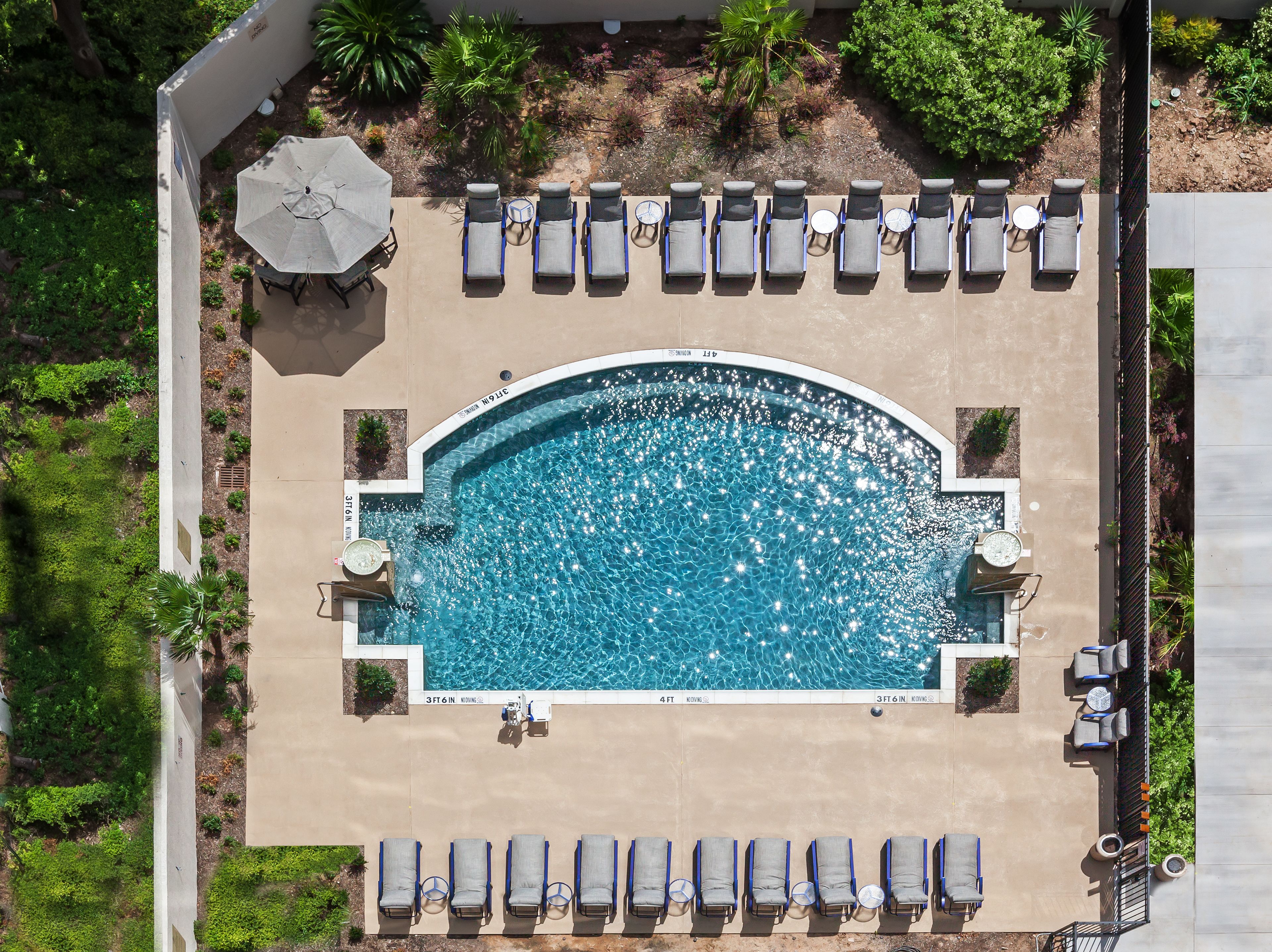 An aerial view of a swimming pool with lounge chairs and umbrellas, surrounded by greenery.