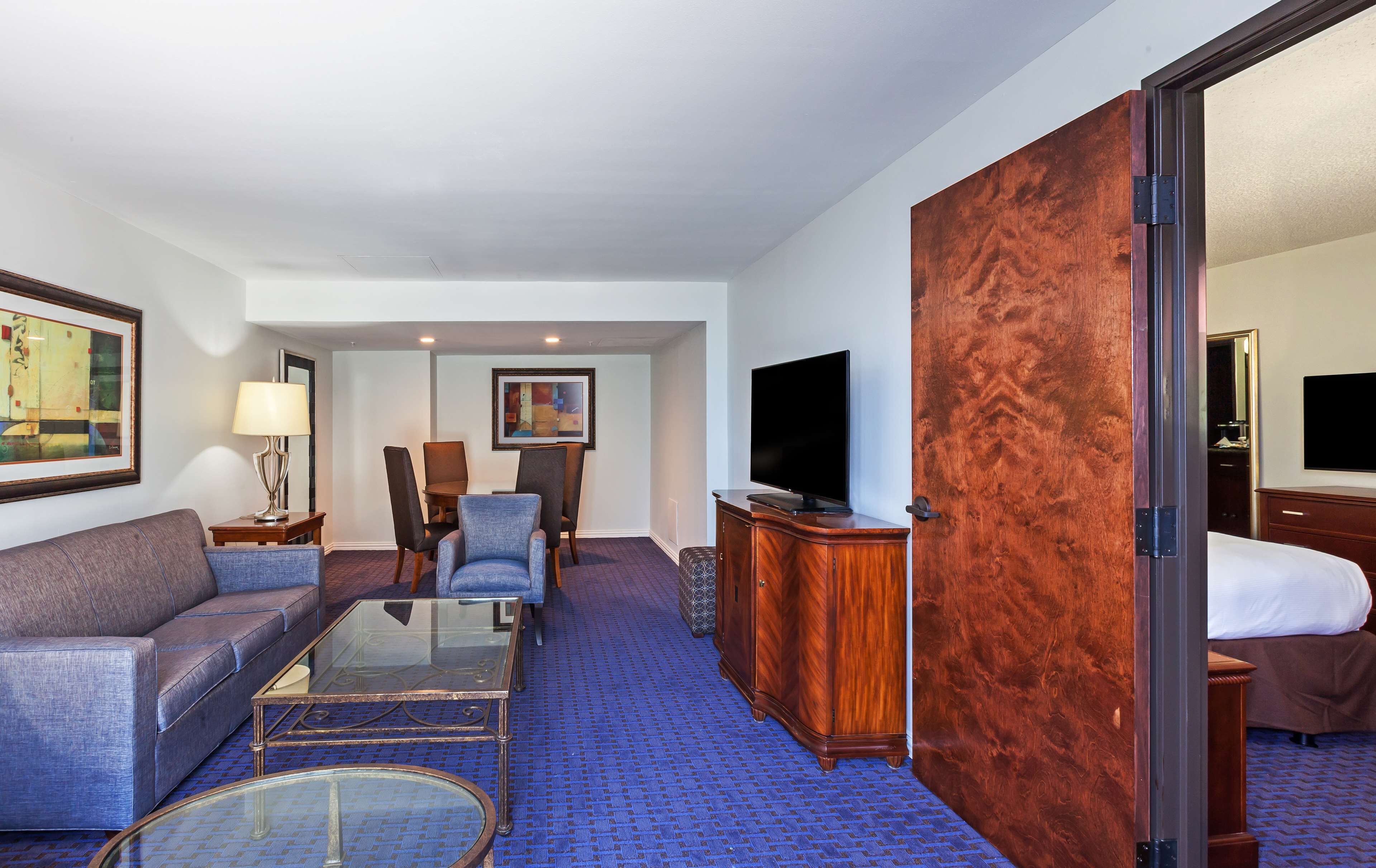 A hotel room with a sofa, armchair, a glass coffee table, a TV, and a wooden wardrobe.