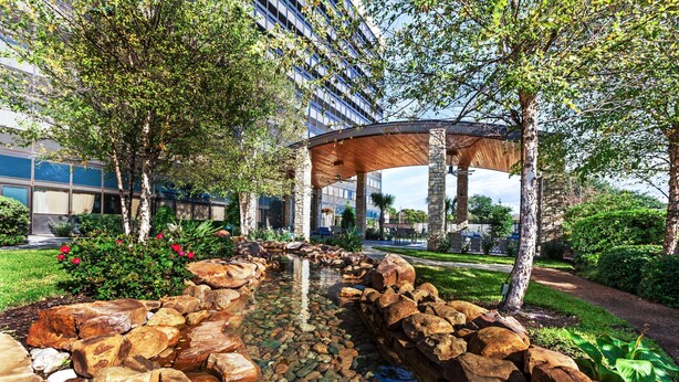 A landscaped garden with a water feature, large rocks, and a wooden pergola. - Hilton Waco (Waco)