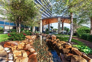 Ein angelegter Garten mit Wasserspiel, großen Steinen und einer hölzernen Pergola.