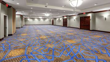 Un amplio salón de conferencias vacío con alfombra estampada, puertas de madera e iluminación empotrada.