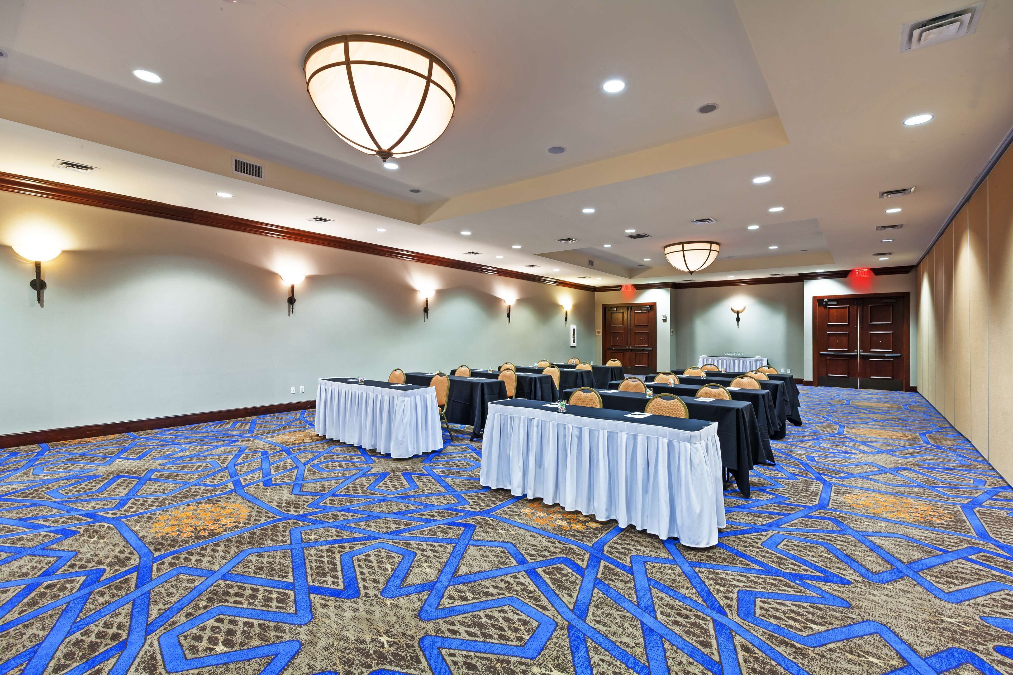 Une salle de conférence avec des tables disposées pour une réunion, équipée de chaises et de tables, et recouverte d’un tapis à motifs.