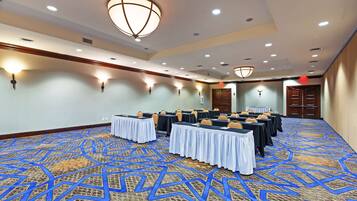 Une salle de conférence avec des tables disposées pour une réunion, équipée de chaises et de tables, et recouverte d’un tapis à motifs.