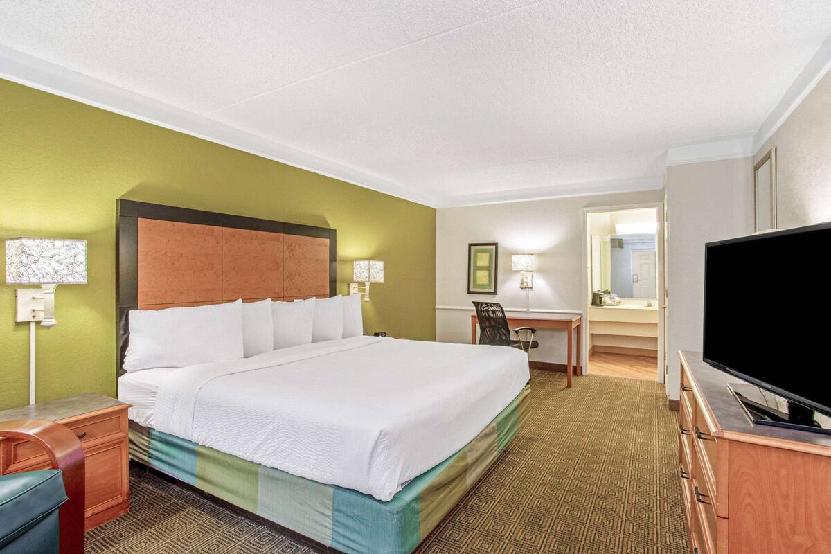 A hotel room with a large bed, a desk, a television, and a bathroom visible through an open door.