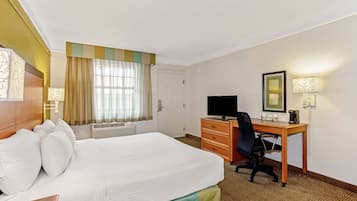 A hotel room with a large bed, a desk with a chair, a television, and a lamp.