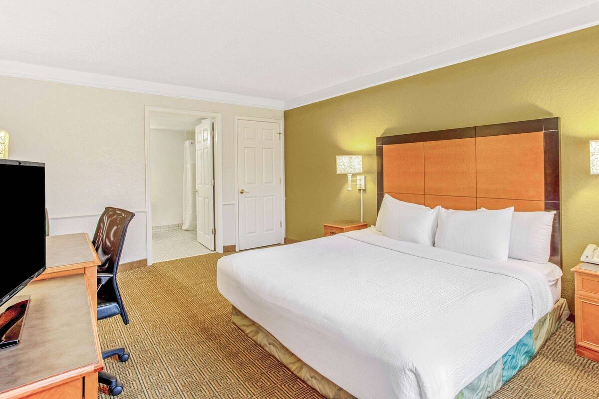 A hotel room with a large bed, a desk with a computer, a chair, and a television.