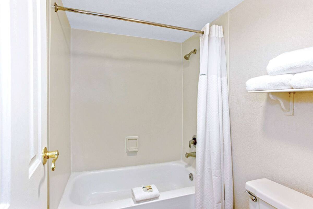 A bathroom with a bathtub, a shower curtain, a towel rack with towels, and a toilet.