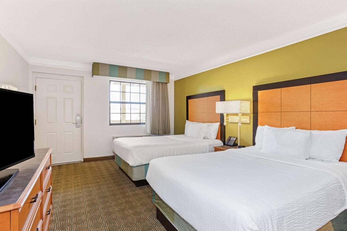 A hotel room with two beds, a television, and a window with curtains.