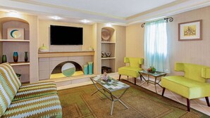 Una sala de estar con sofá, sillones, una mesita de centro, televisor de pantalla plana y adornos.