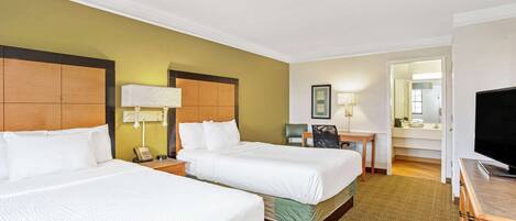 A hotel room with two beds, a desk, a chair, a television, and a bathroom visible through an open door.