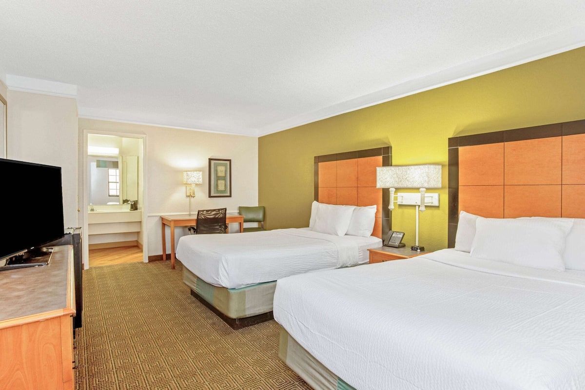 A hotel room with two beds, a TV, a desk, and a chair.