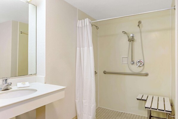 A bathroom with a white sink, a shower with a handheld showerhead, a grab bar, and a towel rack.