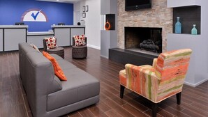 A modern lobby with a reception desk, a grey sofa, a colorful armchair, a fireplace, and a mounted TV.