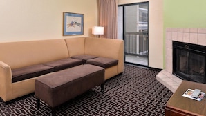 Ein Hotelzimmer mit beiger Couch, Kamin, einem gemusterten Boden und einer Tür, die auf einen Balkon führt.