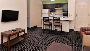 Ein kompaktes Hotelzimmer mit Küchenzeile, Flachbildfernseher, kleinem Tisch und einem gemusterten Teppich.