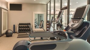 A modern gym with cardio equipment, weight racks, and a large mirror.