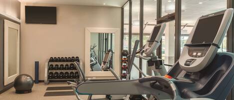A modern gym with cardio equipment, weight racks, and a large mirror.