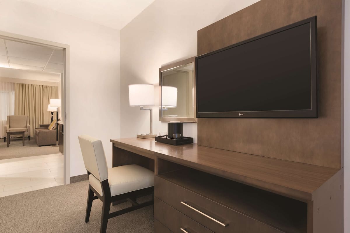 Une chambre d’hôtel équipée d’un bureau en bois, d’une chaise, d’un téléviseur à écran plat et d’une lampe.