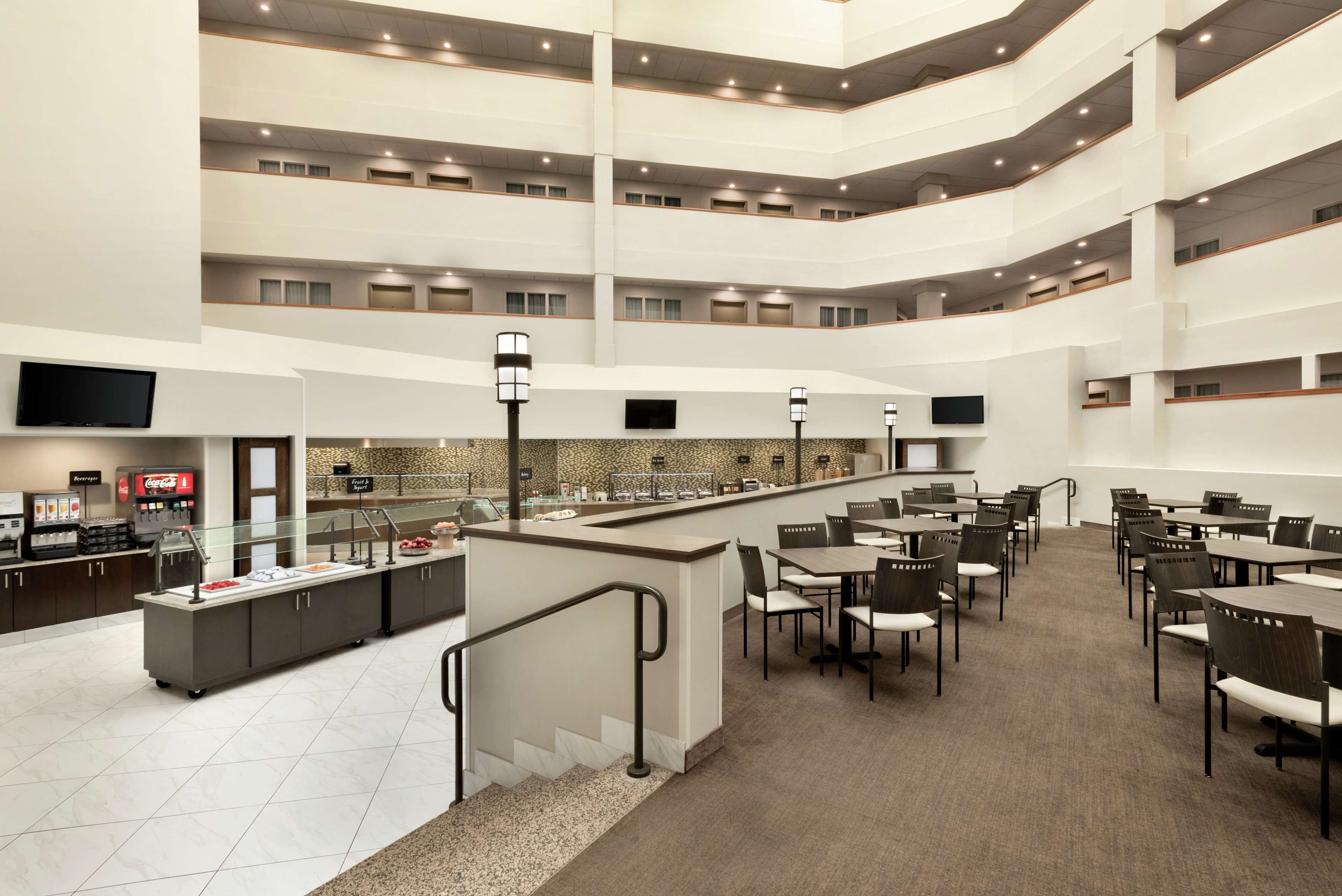 A multi-level hotel lobby with a central bar, dining area, and a Coca-Cola refrigerator.