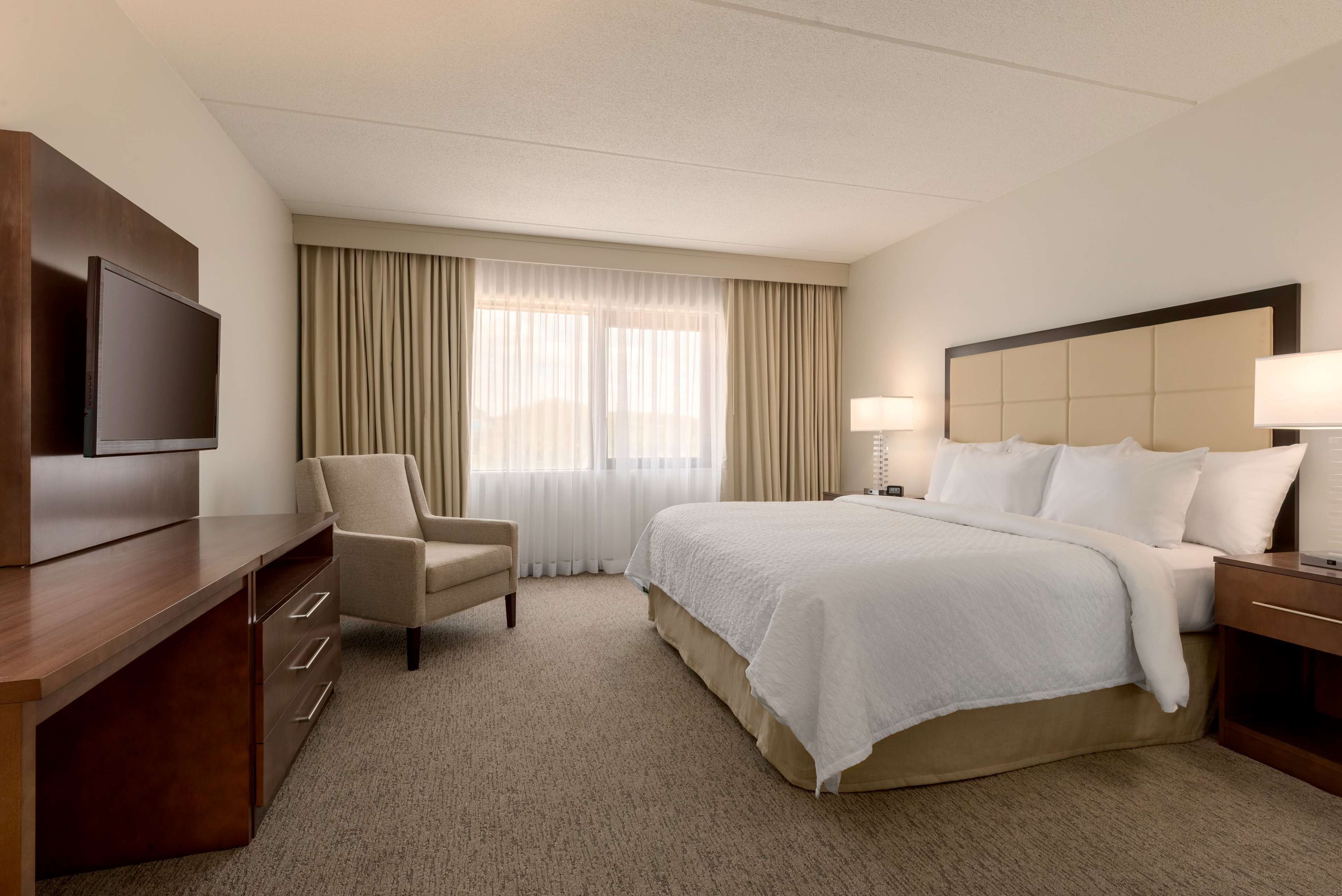 A hotel room with a bed, a desk, a chair, a TV, and a window with curtains.