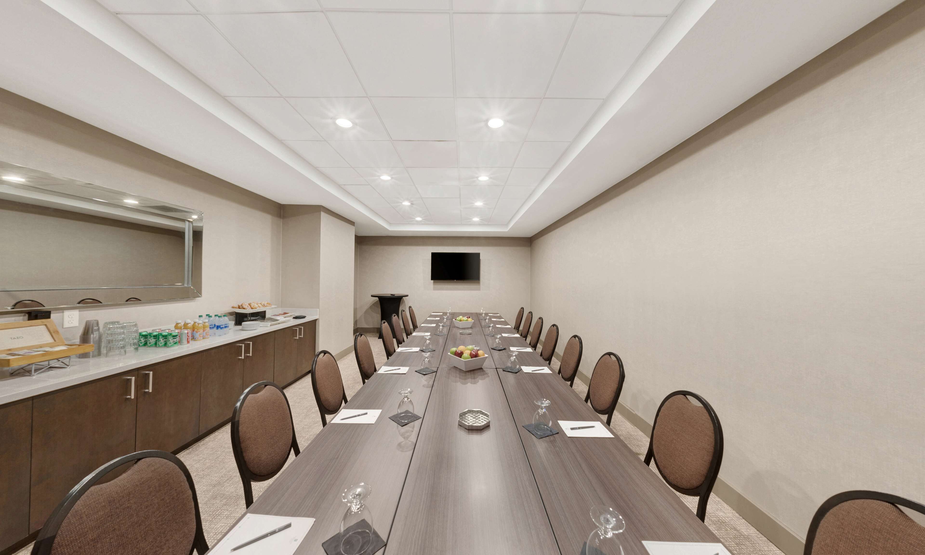Un salón de conferencias con una larga mesa, sillas, una pantalla de televisión y un mostrador con bebidas.