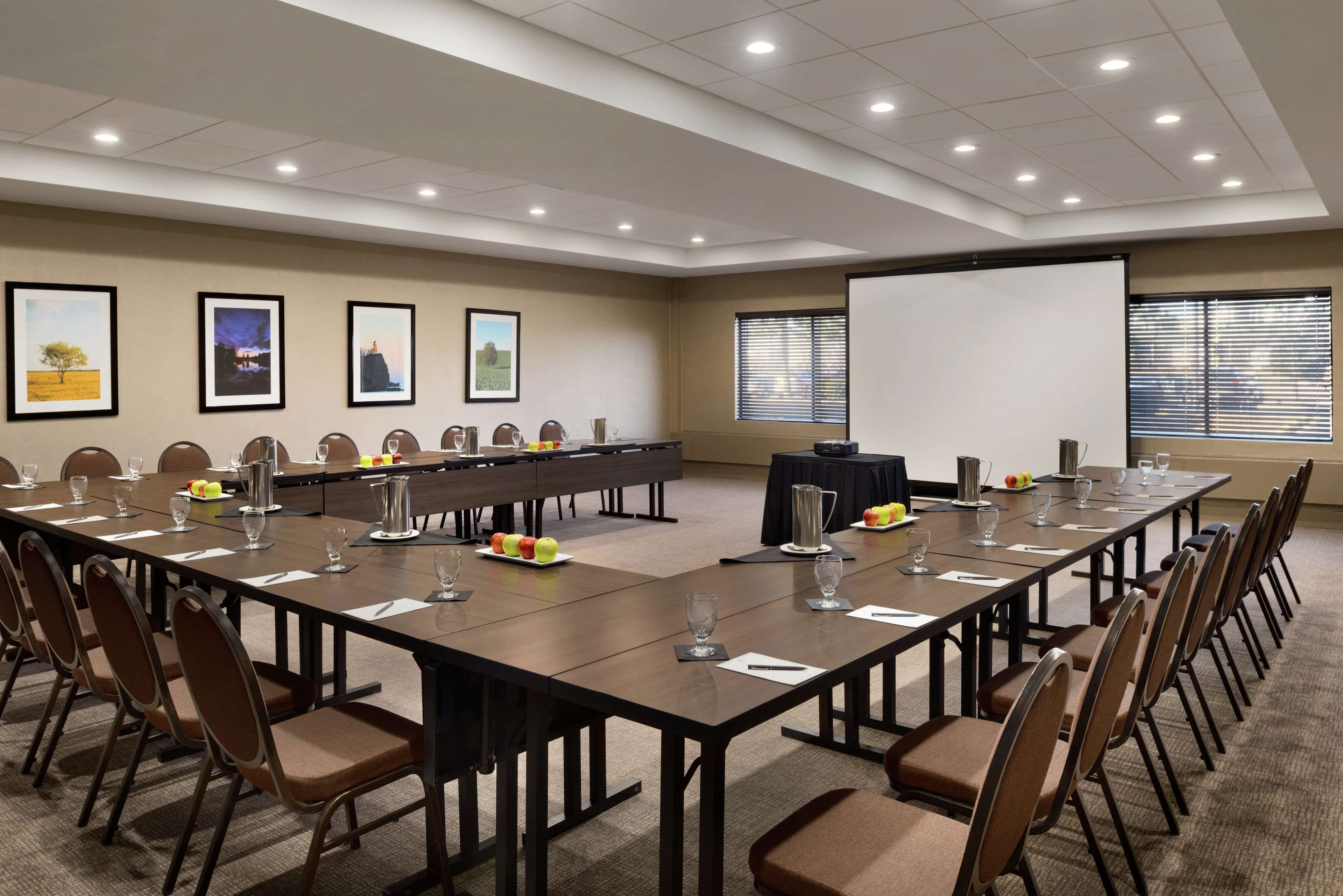 A conference room with a long table, chairs, a projector screen, and framed pictures on the wall.