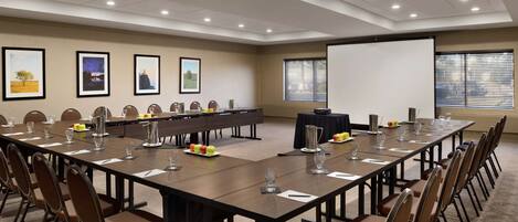 A conference room with a long table, chairs, a projector screen, and framed pictures on the wall.