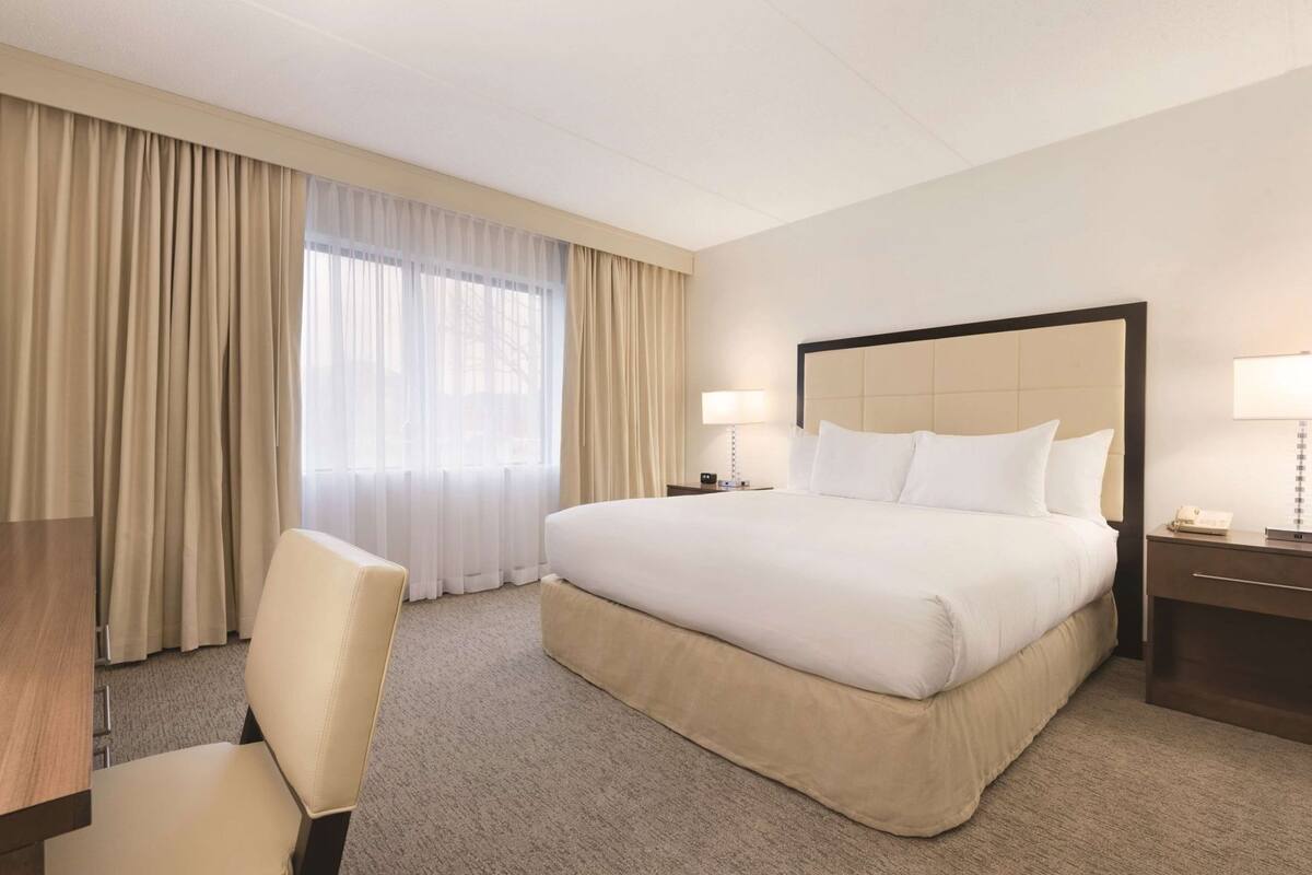 Une chambre d’hôtel avec un grand lit, un bureau, une chaise, une table de chevet et une lampe.