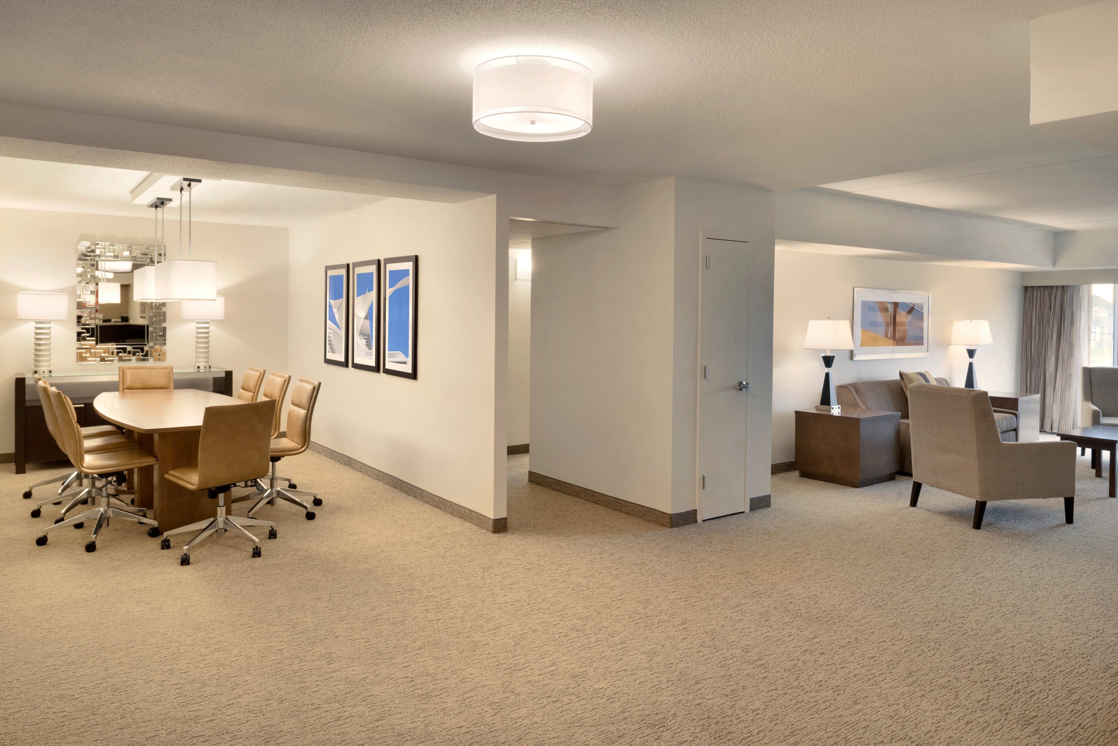 Habitación de hotel con comedor, un conjunto de sofás y un escritorio con lámpara.